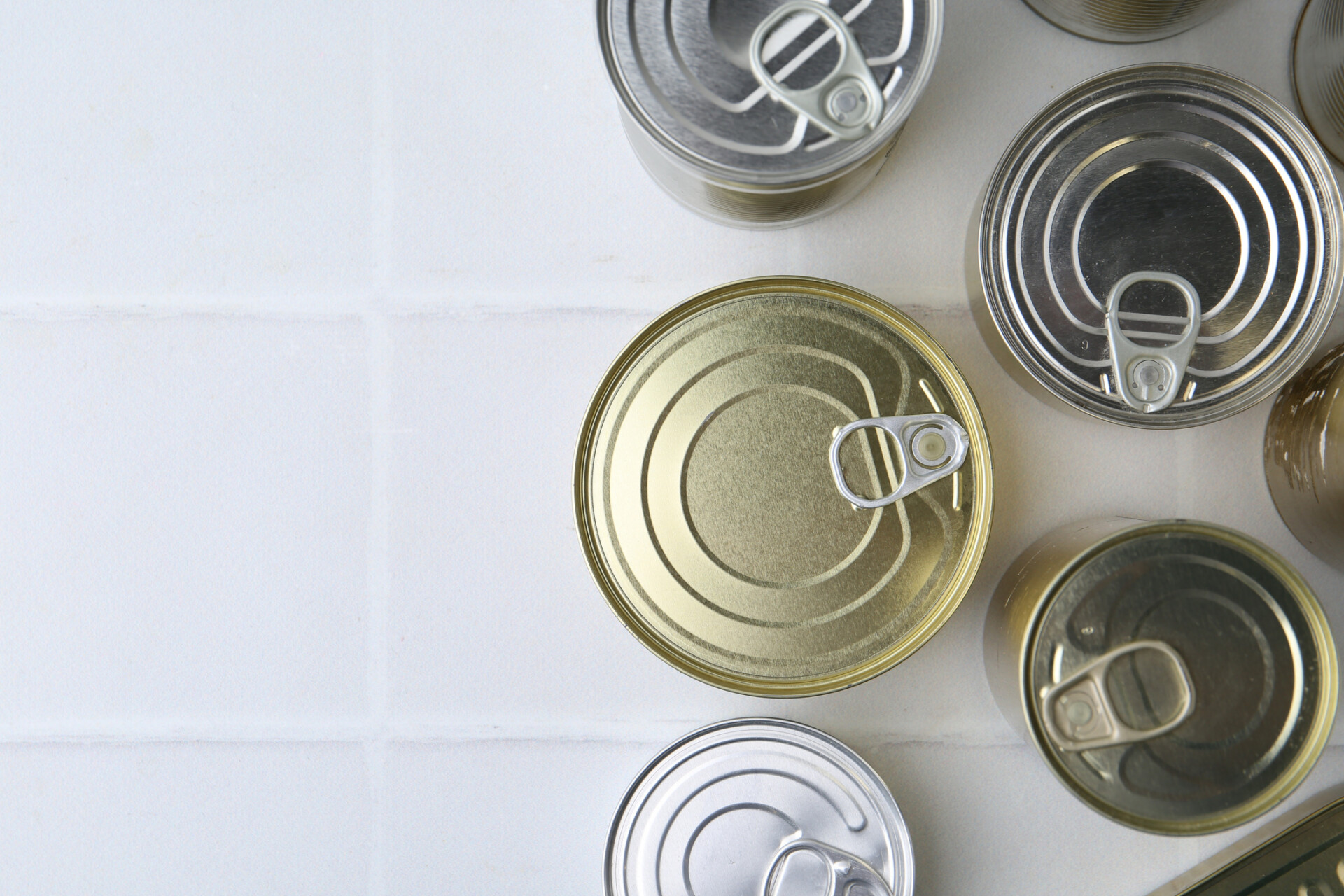 Many closed tin cans on white tiled table flat lay Space for text | 金屬包裝容器製造 | 三片式鐵罐製造 | 中國製罐金屬股份有限公司